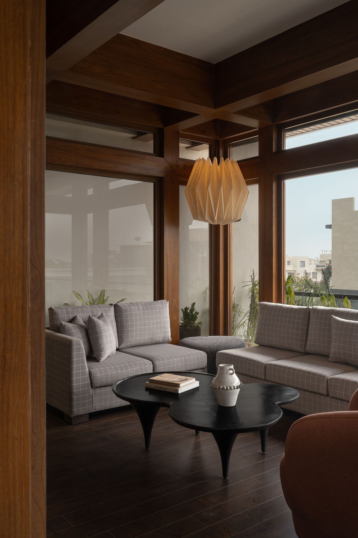 Contemporary lounge with plaid sofas, origami pendant light, dark wood beams, and floor-to-ceiling windows.