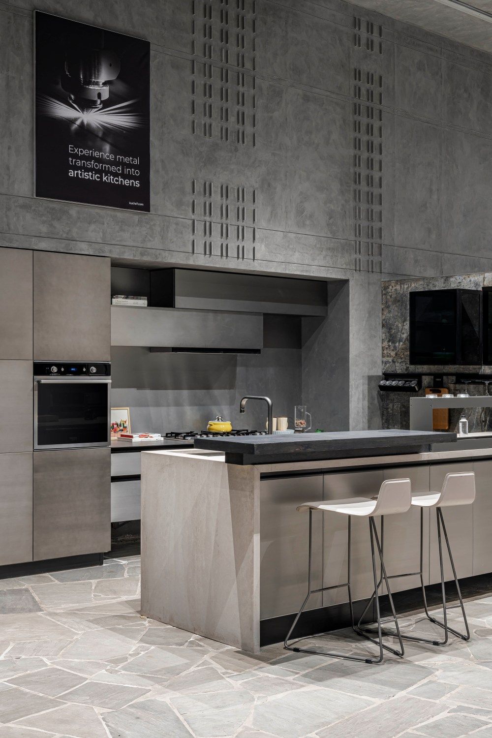 Modern grey kitchen with island, bar stools, built-in oven, and artistic metal wall decor.
