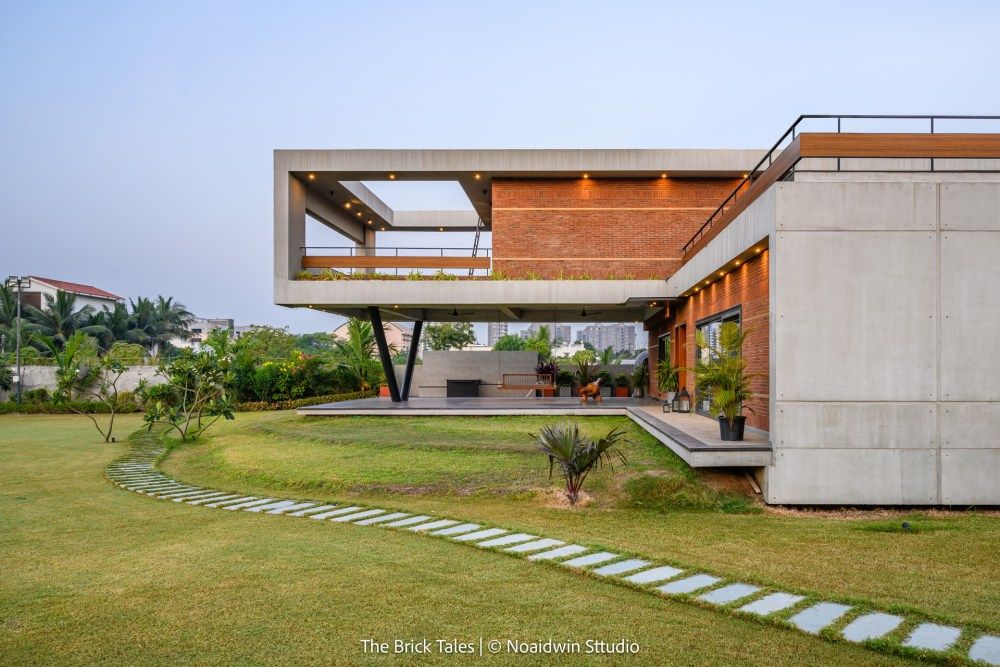 Contemporary concrete and brick residence with cantilevered roof, open terrace, and manicured lawn at dusk.