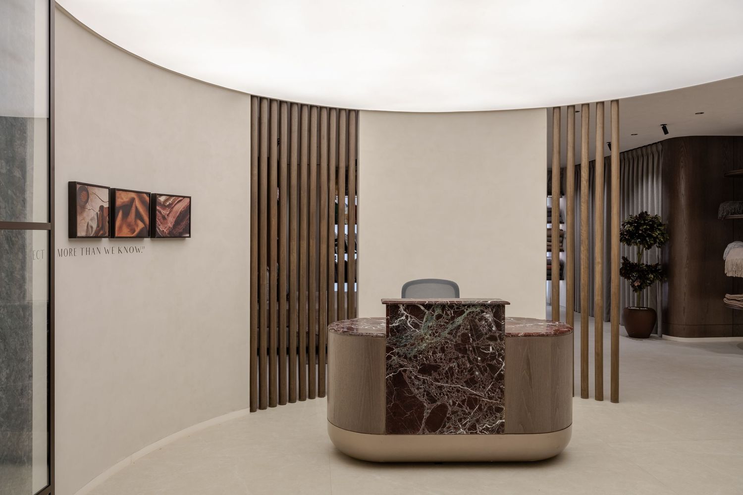 Curved reception area with marble desk, vertical wood slats, and neutral toned walls.