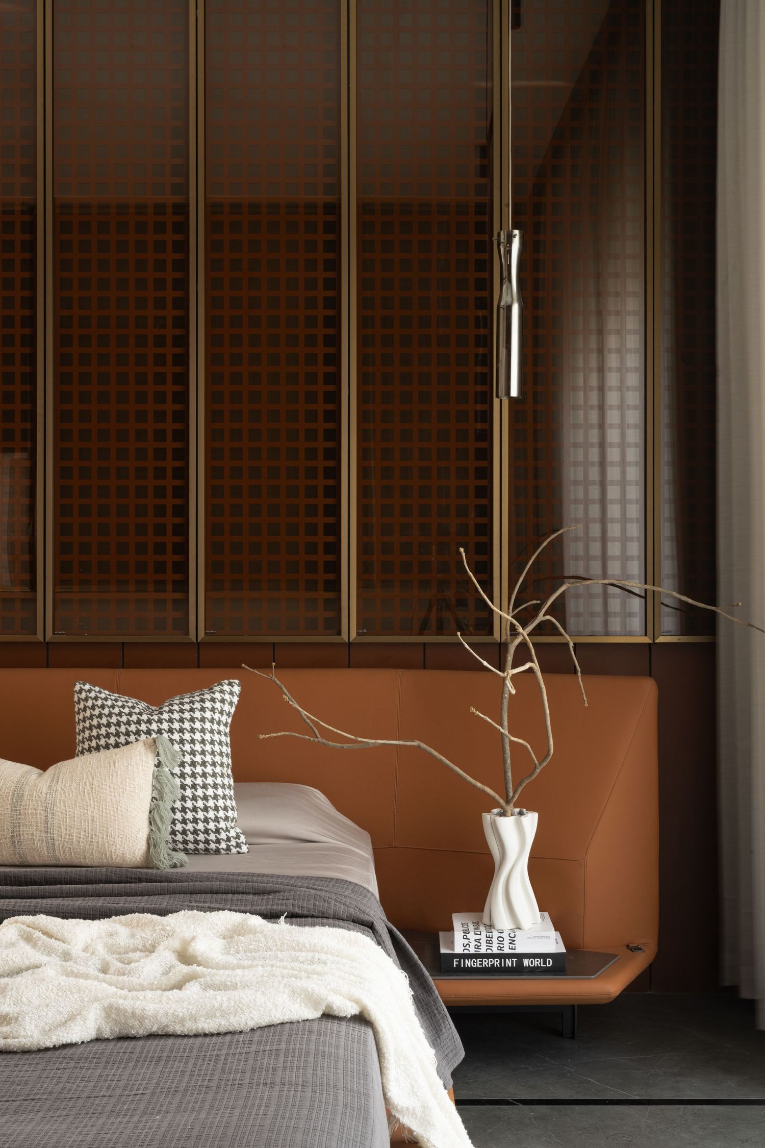 Stylish bedroom with terracotta leather headboard, houndstooth pillow, brass grid wall panel, and ceramic vase.