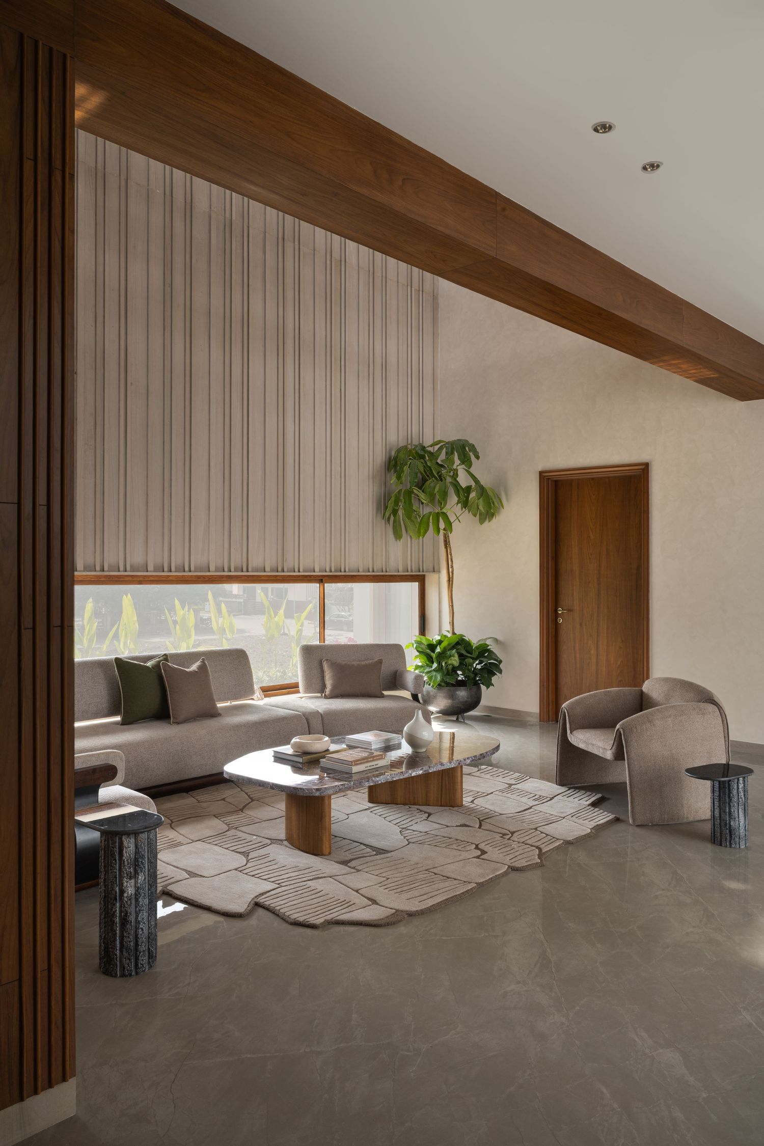 Minimalist living room with neutral sofa, organic stone coffee table, wood beams, and indoor plant.