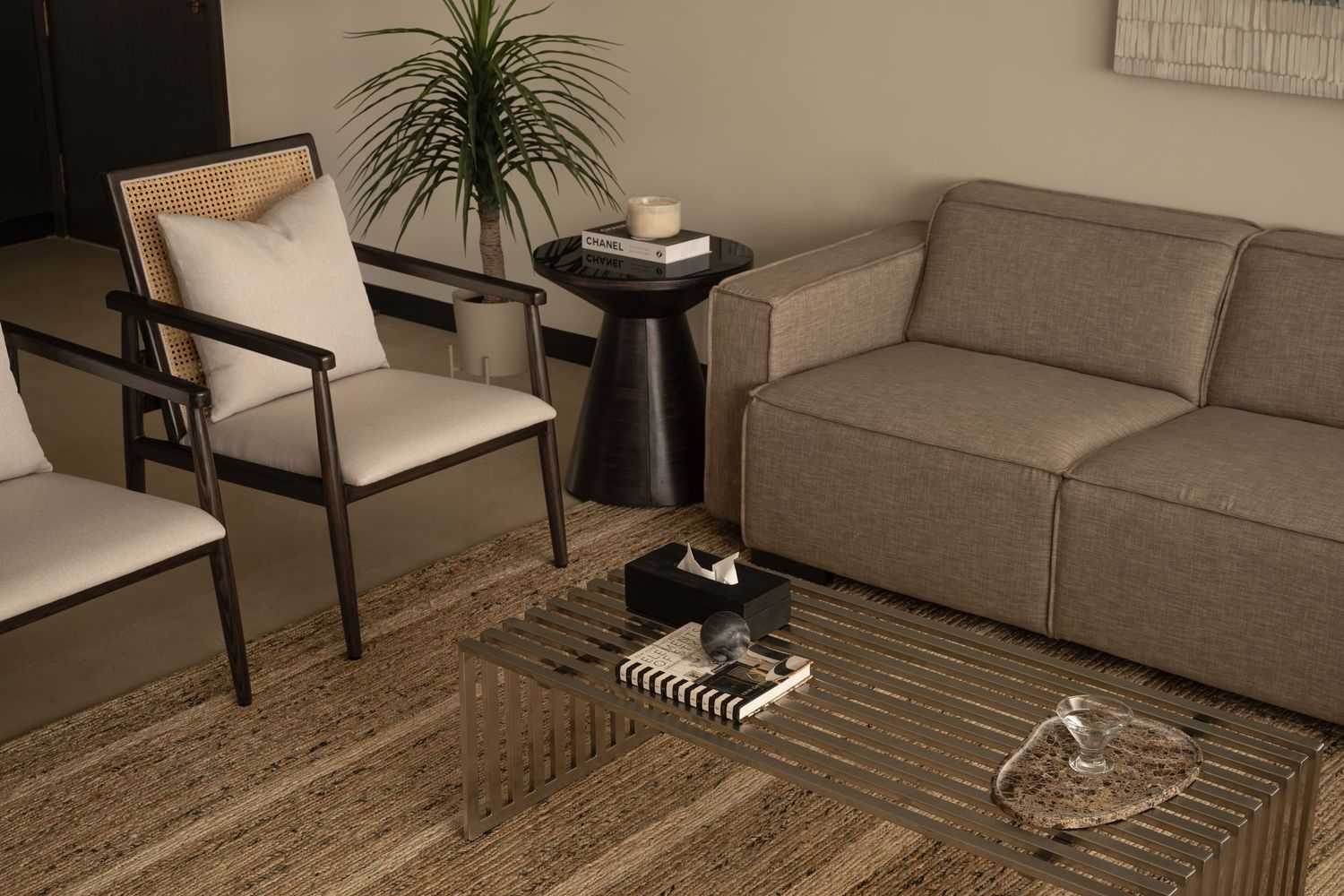Modern living room detail with gray sofa, cane chair, black side table, and striped coffee table.
