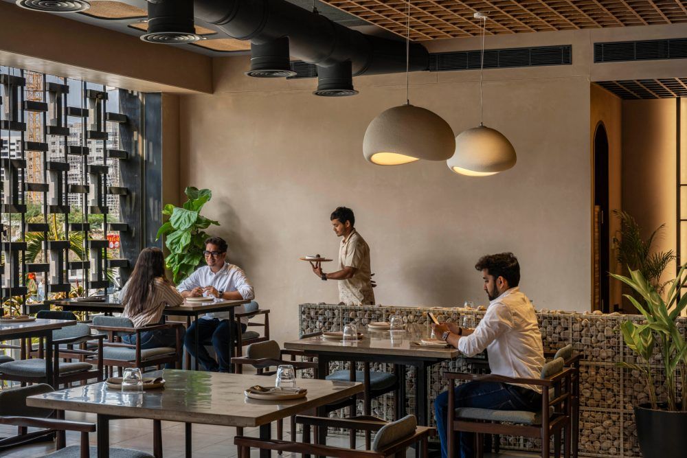 Cozy restaurant interior with pendant lights, wooden furniture, and a waiter serving guests at intimate dining tables.