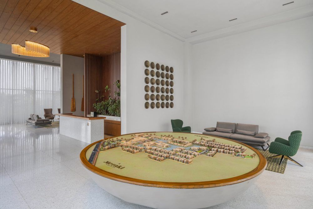 Luxurious living room with round decorative table, wooden ceiling, green accent chairs, and gold disc wall art.