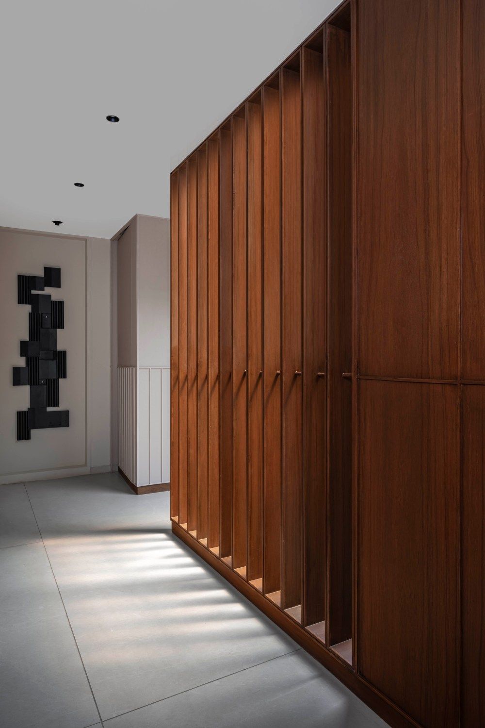 Luxury interior hallway with floor-to-ceiling walnut wood slatted cabinet wall and abstract black wall sculpture.