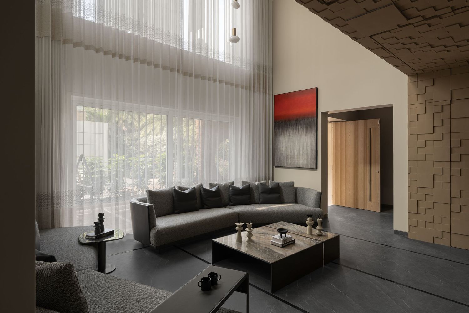Modern living room with gray sectional sofa, sheer white curtains, red abstract art, and textured stone wall.