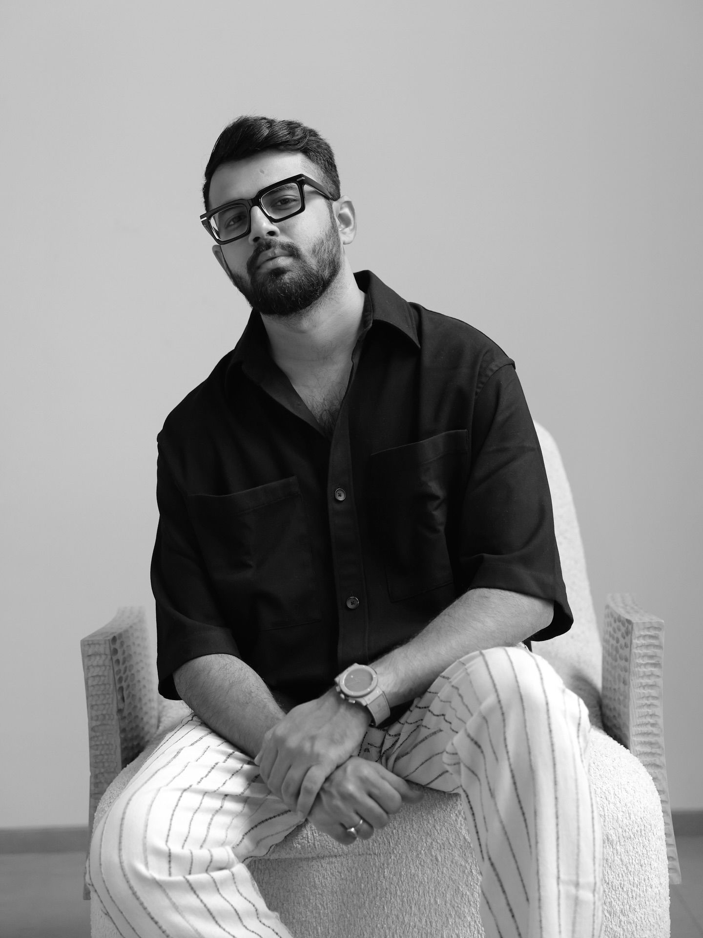 Black and white portrait of a bearded man in glasses and black shirt seated in a chair.