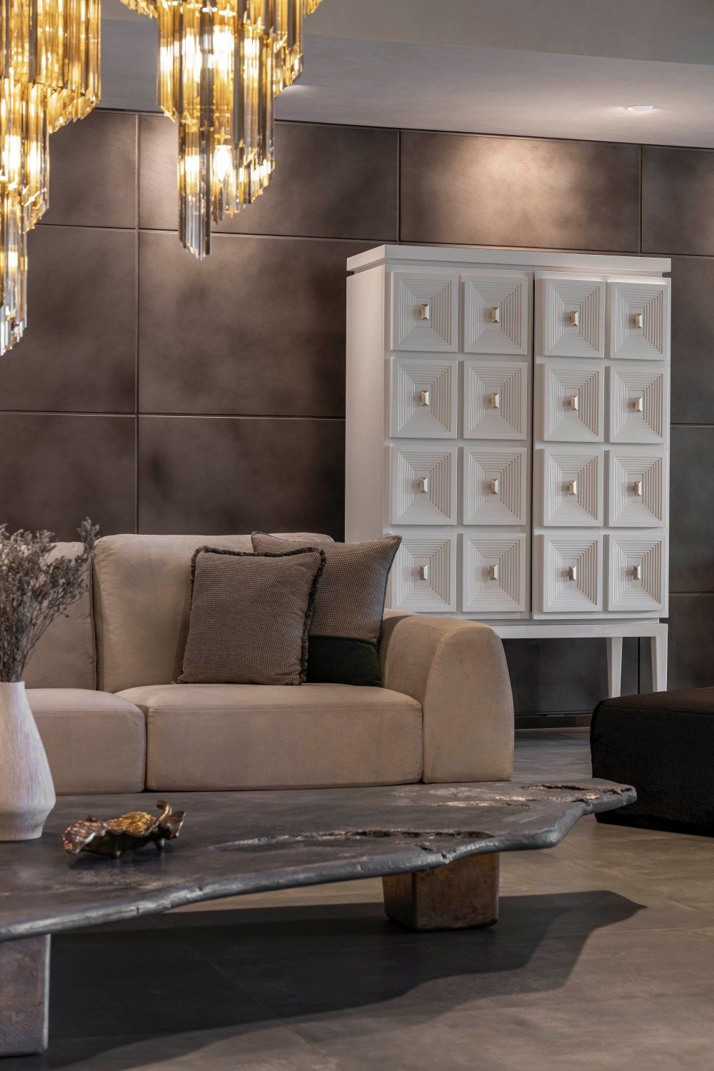 Luxurious living room with beige curved sofa, white geometric cabinet, live-edge coffee table, and gold crystal chandelier.