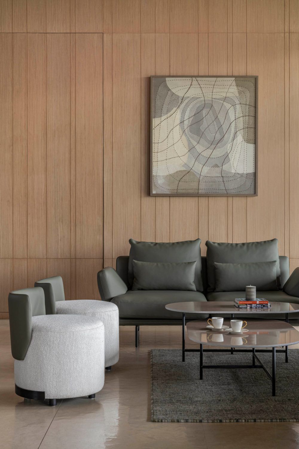 Minimalist lounge with wood panel wall, olive green sofa, white accent chair, abstract art, and marble coffee table.