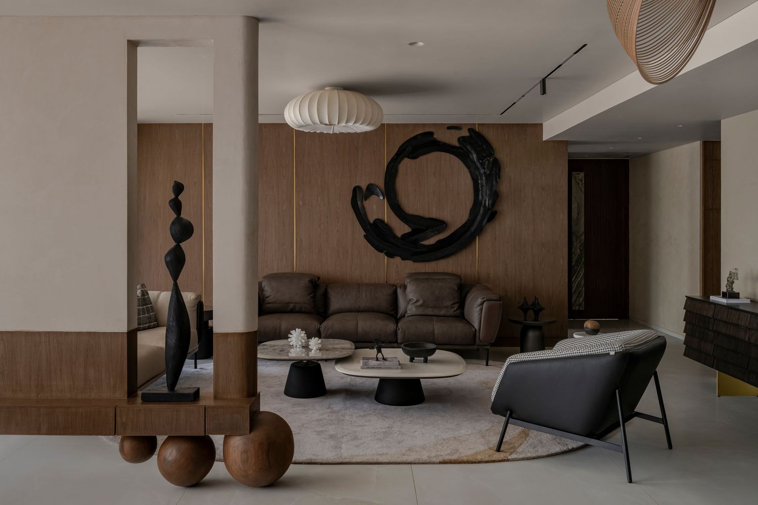 Contemporary living room with dark wood paneling, large circular black brushstroke artwork, sculptural decor, and minimalist furniture.