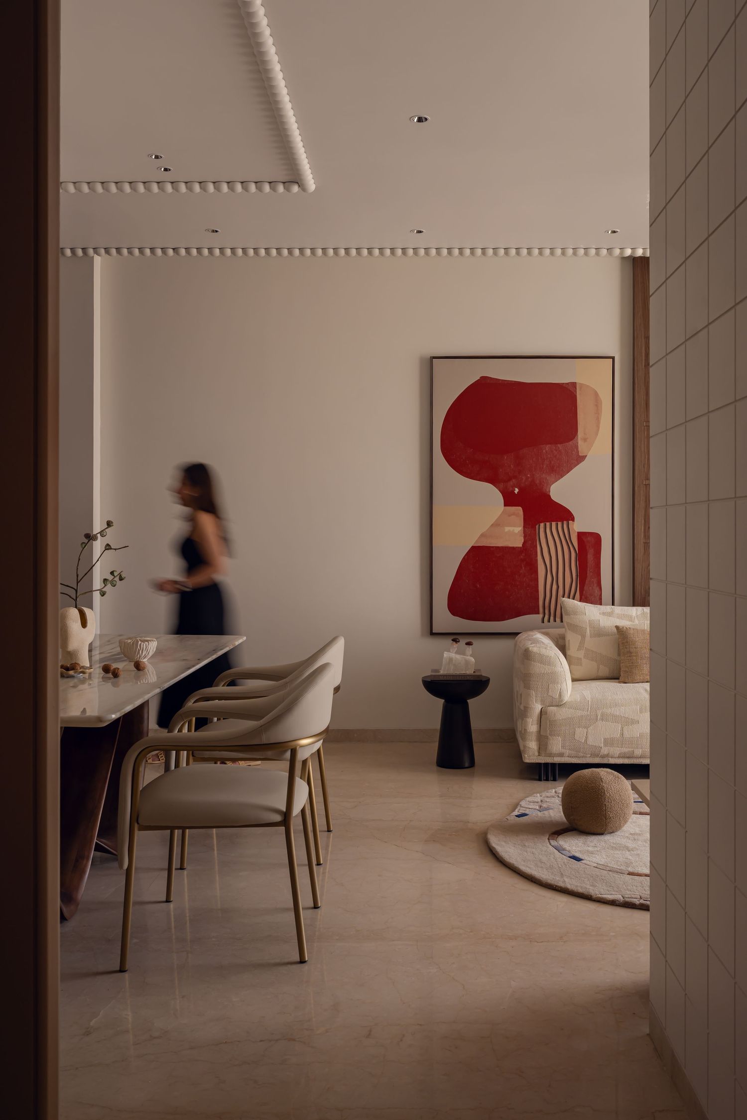 Open plan interior with cream sofa, bold red artwork, dining area with gold chairs, and marble table.