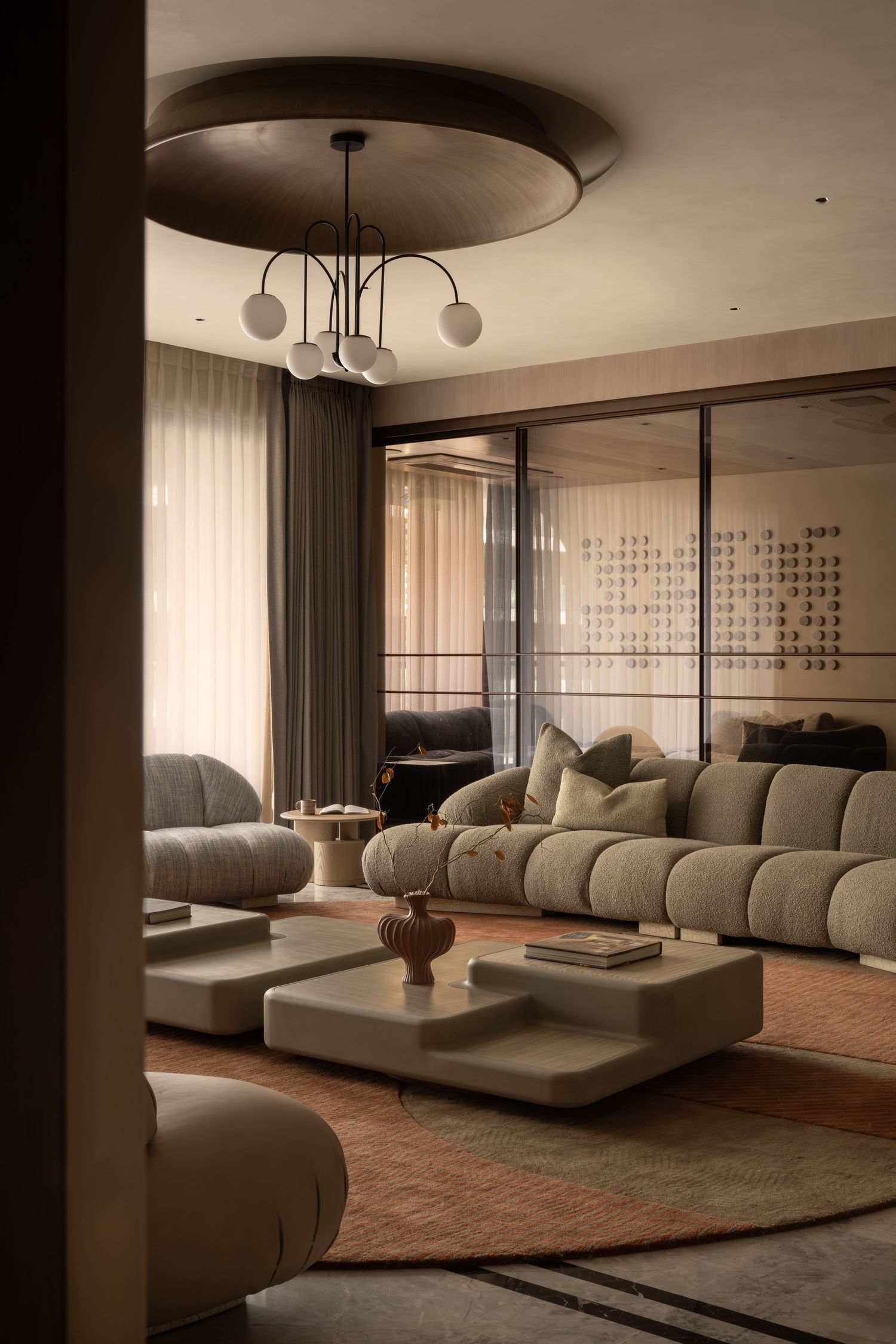 Sophisticated living room with modular gray sofas, white coffee tables, globe chandelier, and sheer curtains.