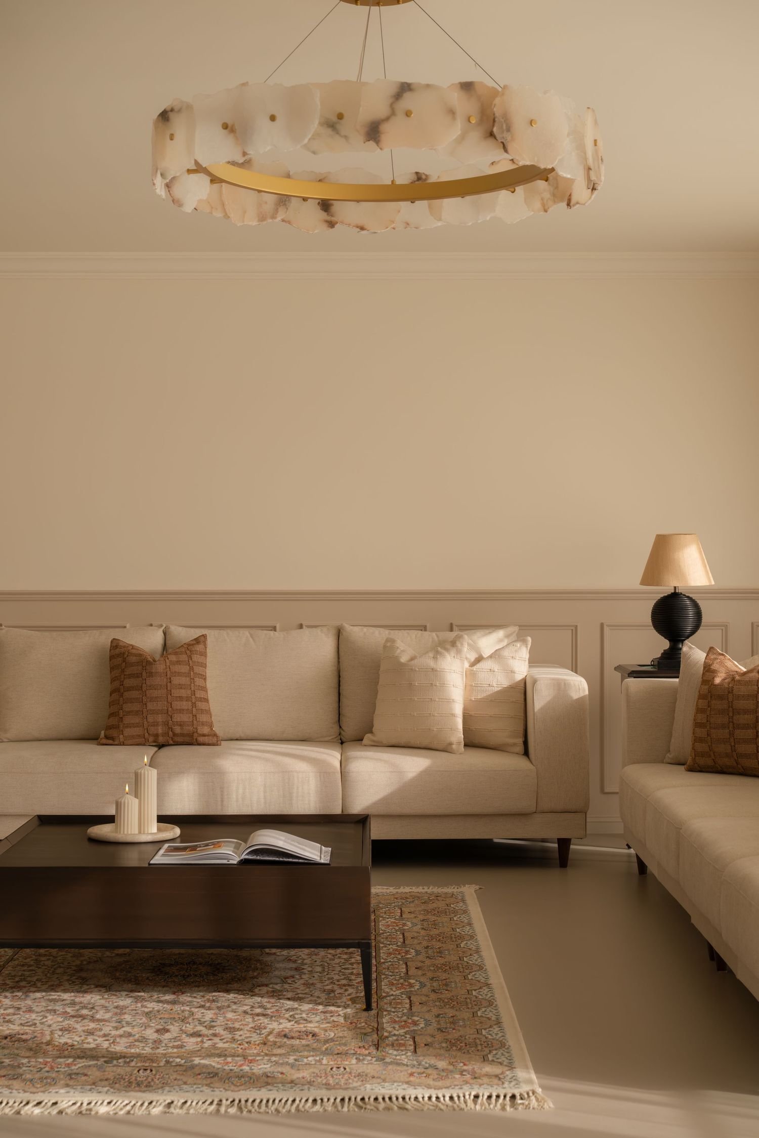 Elegant beige living room with cream sofa, terracotta pillows, dark coffee table, and alabaster chandelier.