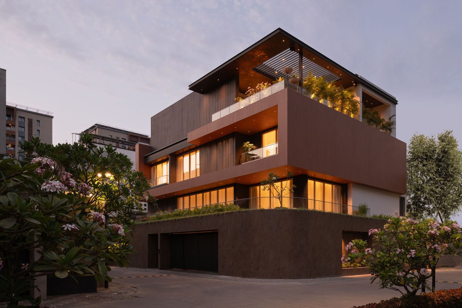 Contemporary multi-level residence featuring warm terracotta tones, large glass windows, and lush garden surroundings.