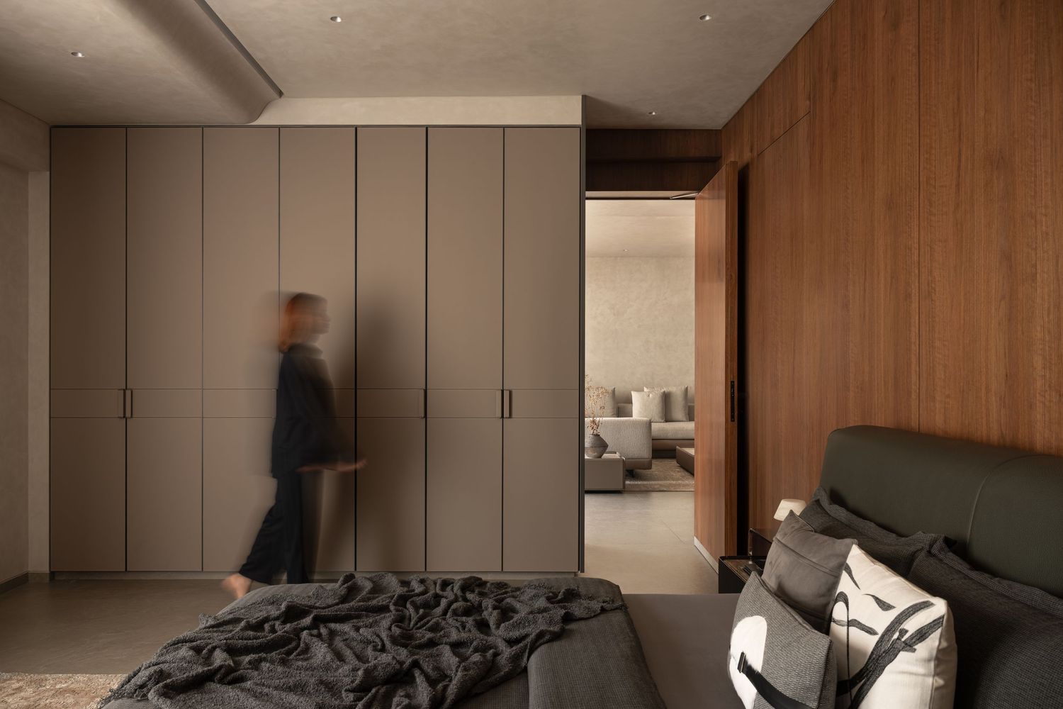 Modern bedroom with floor-to-ceiling taupe wardrobes, dark green upholstered bed, and warm wood panel accent wall.