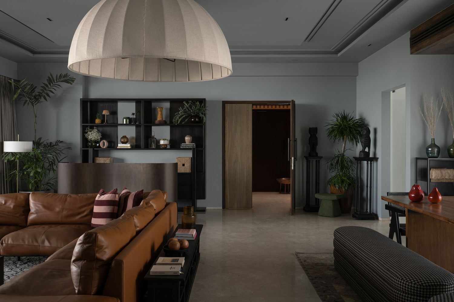Modern living room with leather sofa, large dome pendant light, dark wood shelving, and moody gray walls.
