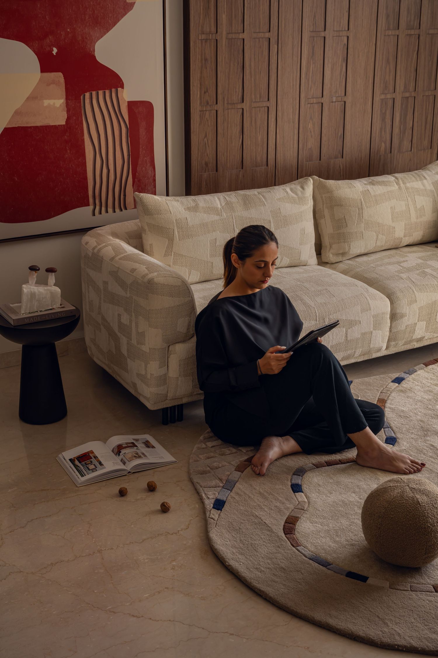 Woman relaxing on floor beside cream textured sofa with red abstract art and round patterned rug in modern living room.