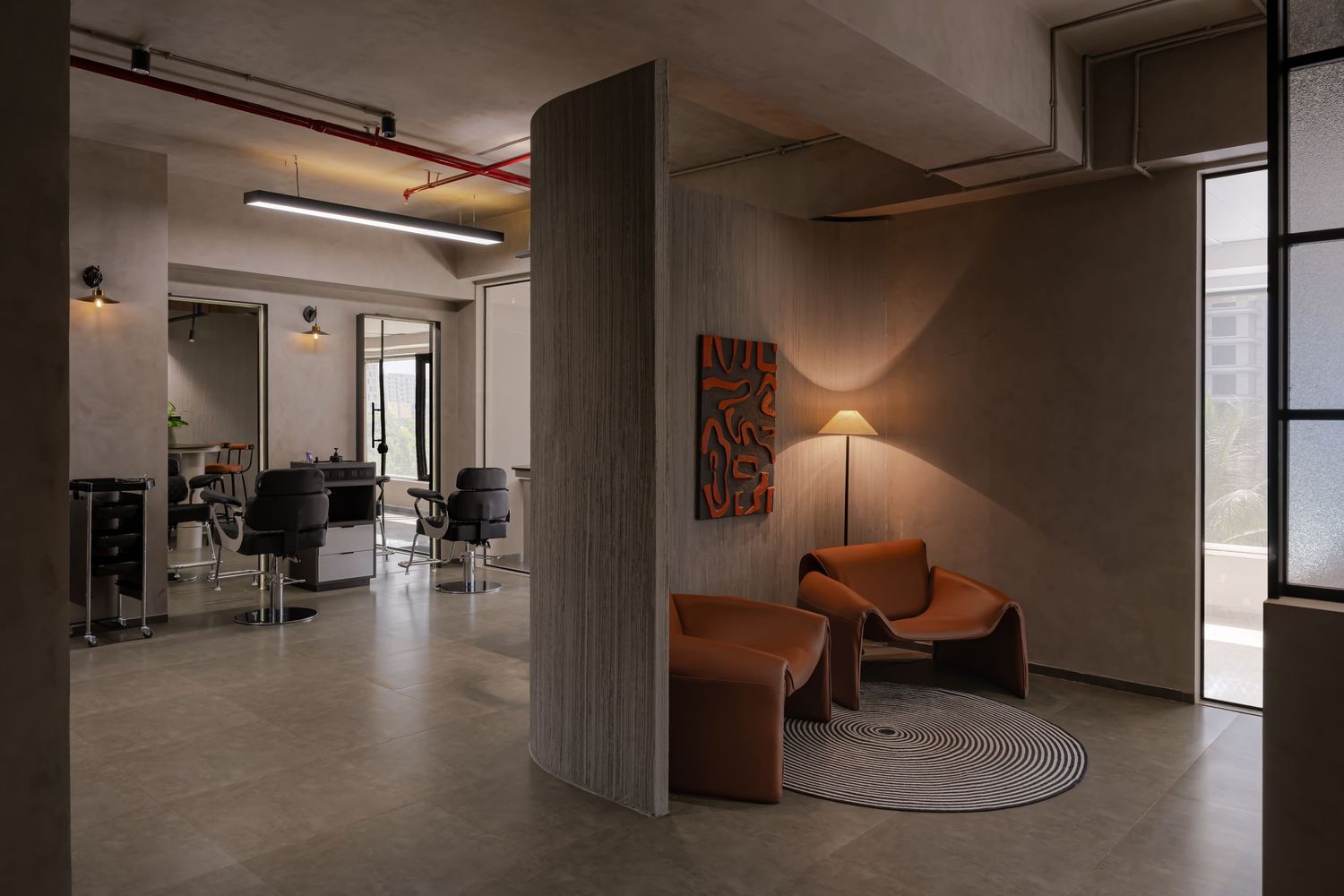 Modern hair salon interior with orange velvet seating area, concrete columns, and styling stations in a minimalist industrial space.