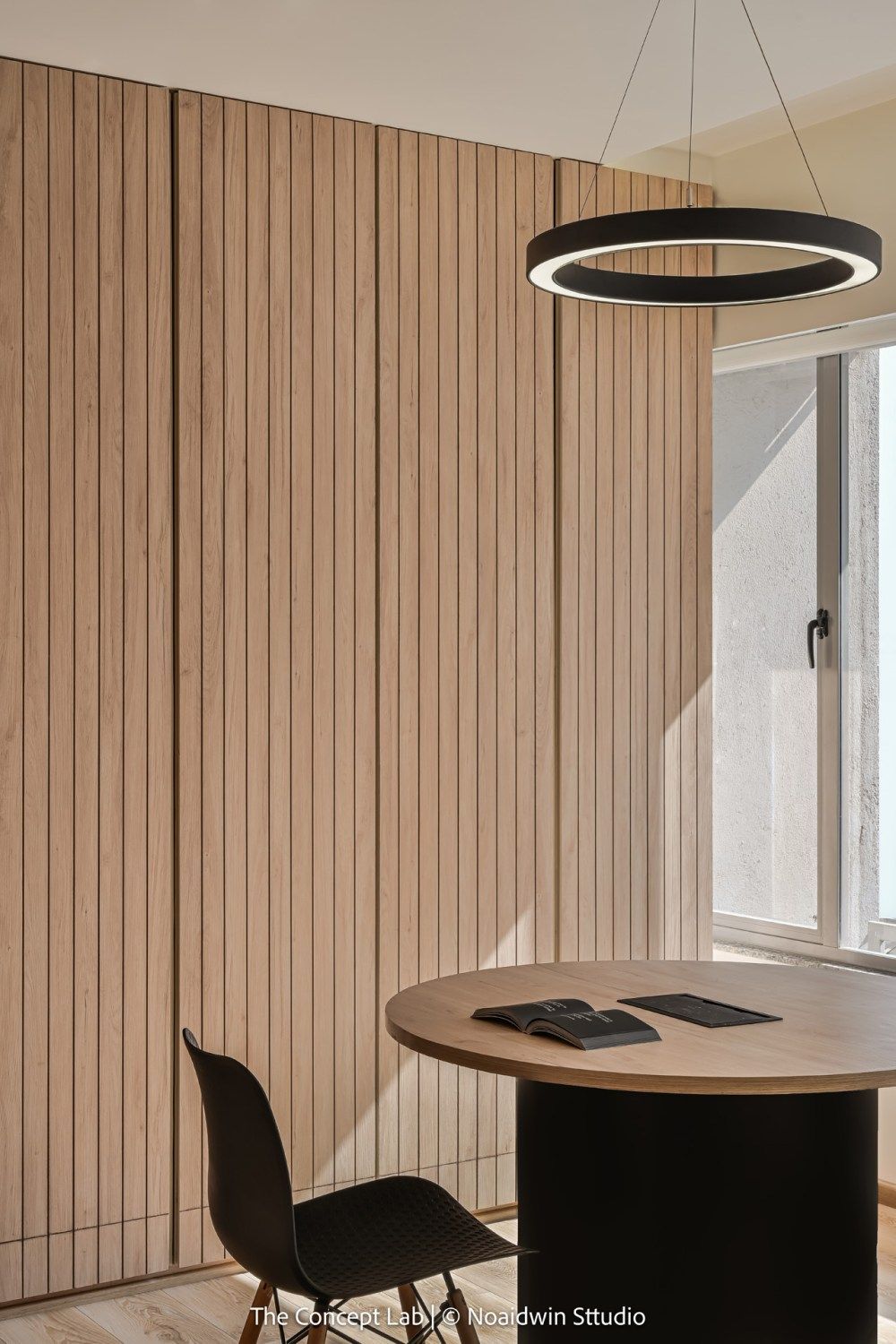 Minimalist meeting room with vertical wood slat wall, round black pendant light, and circular table.