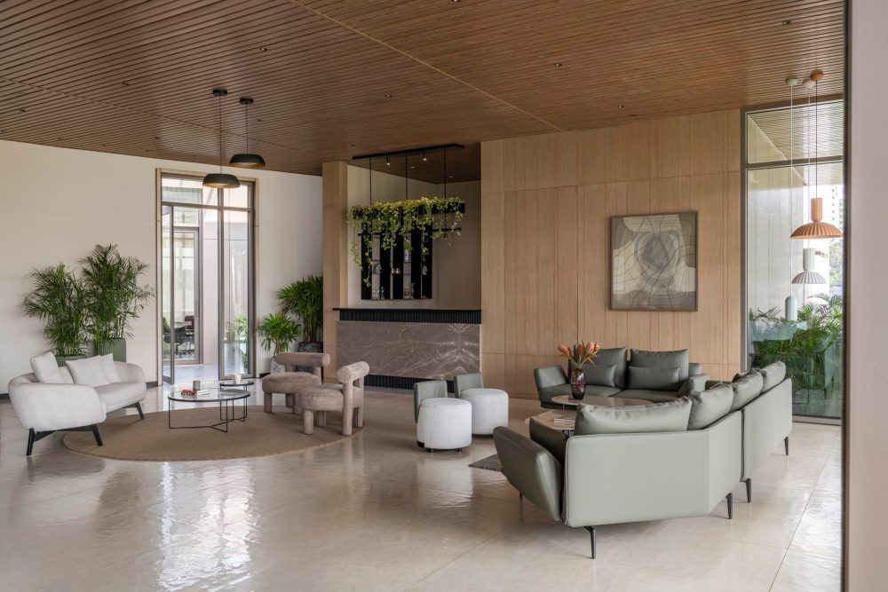 Sophisticated hotel lobby with wood ceiling, green plants, mixed seating arrangements, and marble tile flooring.
