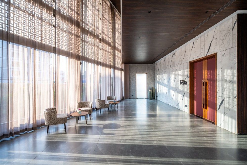 Sunlit hotel lobby with sheer curtains, marble walls, wooden ceiling, and modern lounge seating.