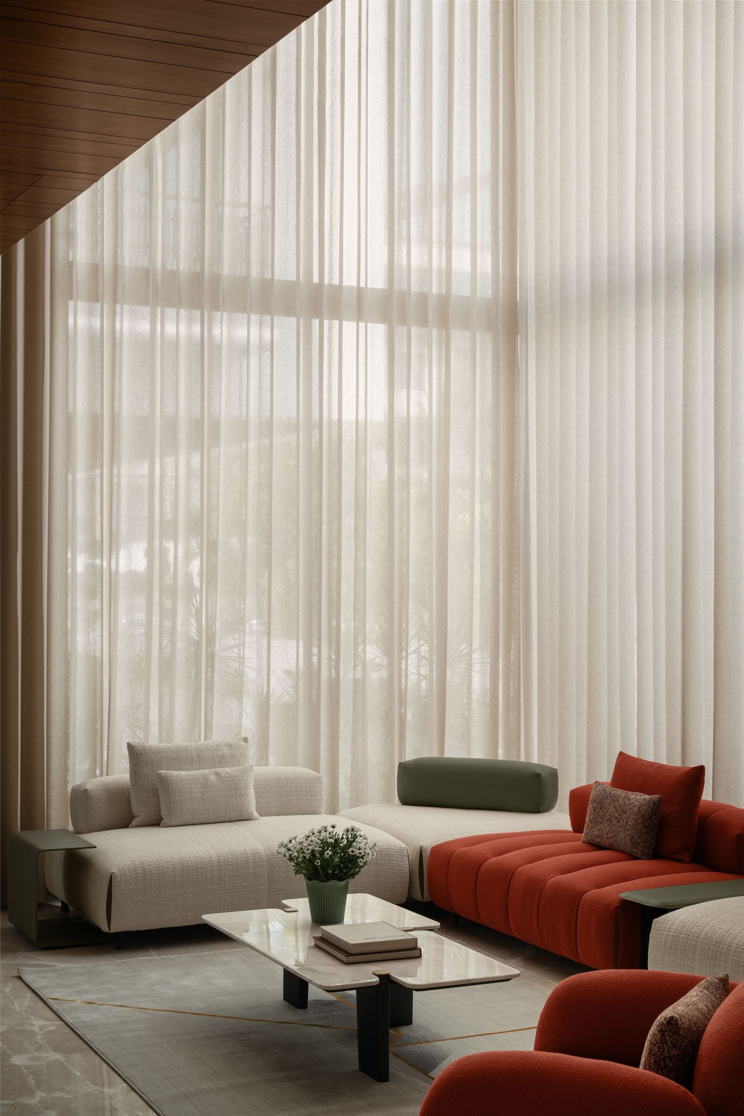Modern living room with floor-to-ceiling sheer curtains, red tufted sofa, cream modular seating, and marble coffee table.