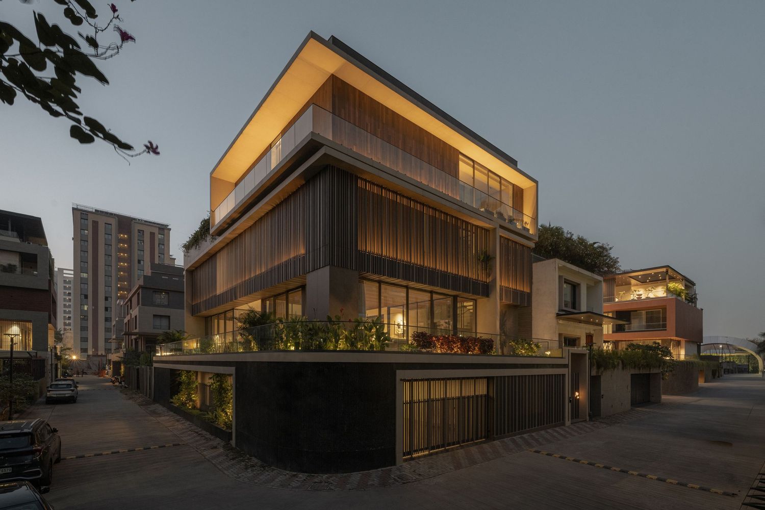 Contemporary multi-story building with vertical wood cladding, green terraces, and dramatic evening lighting.