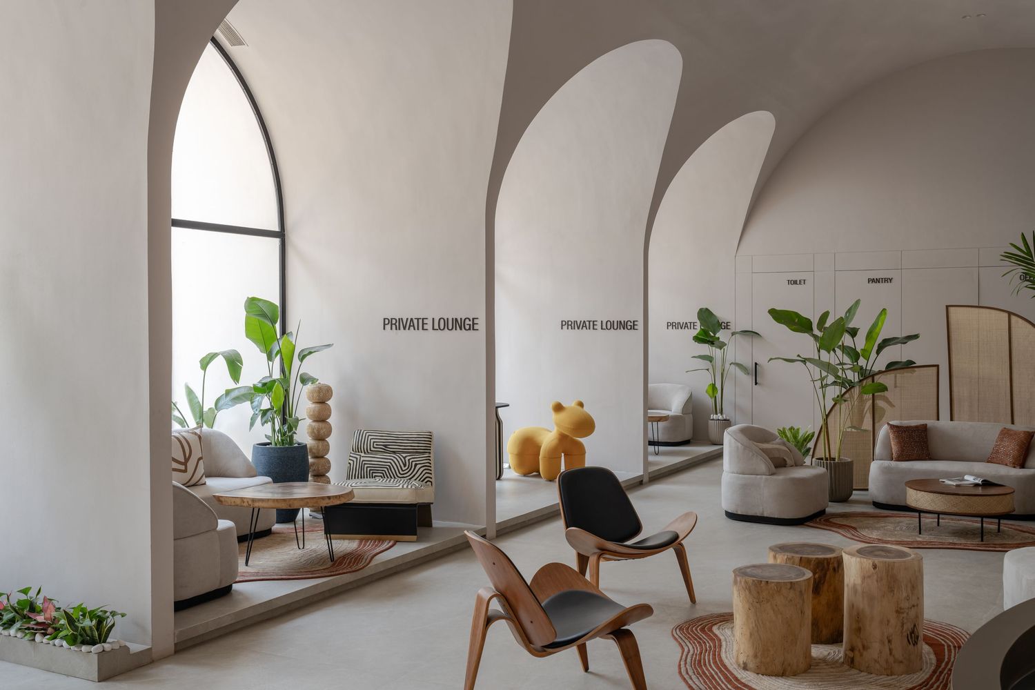 Spacious lounge with dramatic arched openings, natural wood furniture, tropical plants, and soft neutral palette.