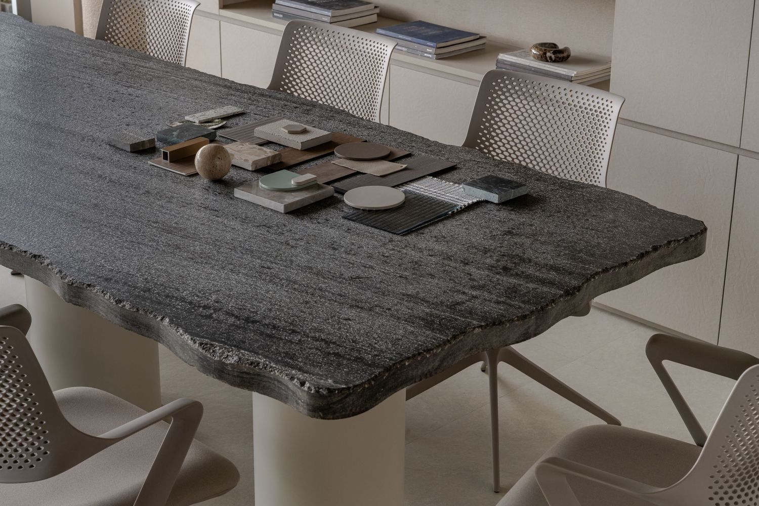Dark granite dining table with live edge detail surrounded by modern white chairs in a contemporary dining room.