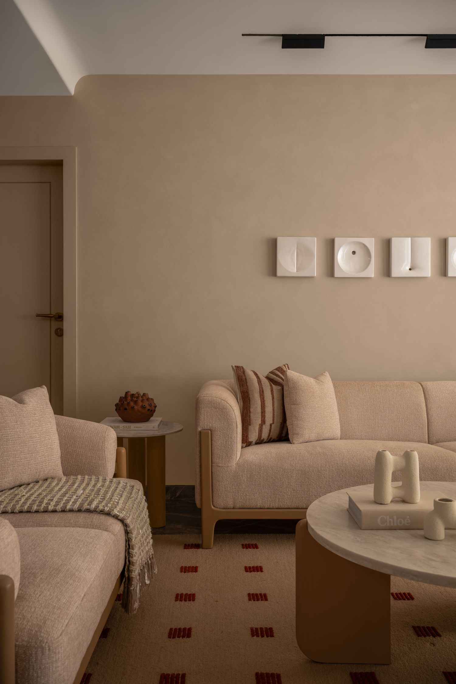 Minimalist living room with beige sofas, round marble coffee table, and abstract wall art panels.