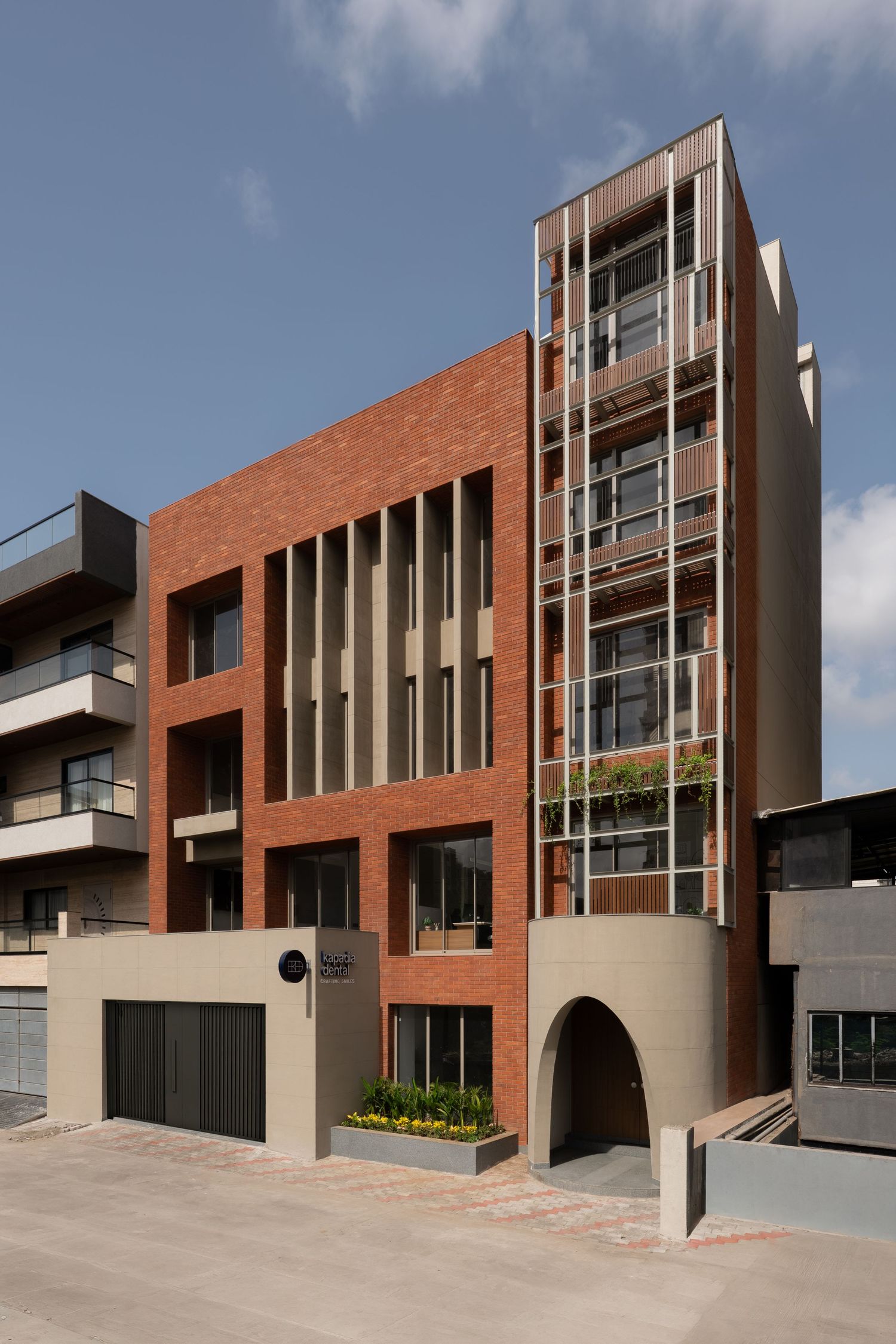 Contemporary multi-story brick apartment building with vertical window panels, arched entry, and landscaped street frontage.