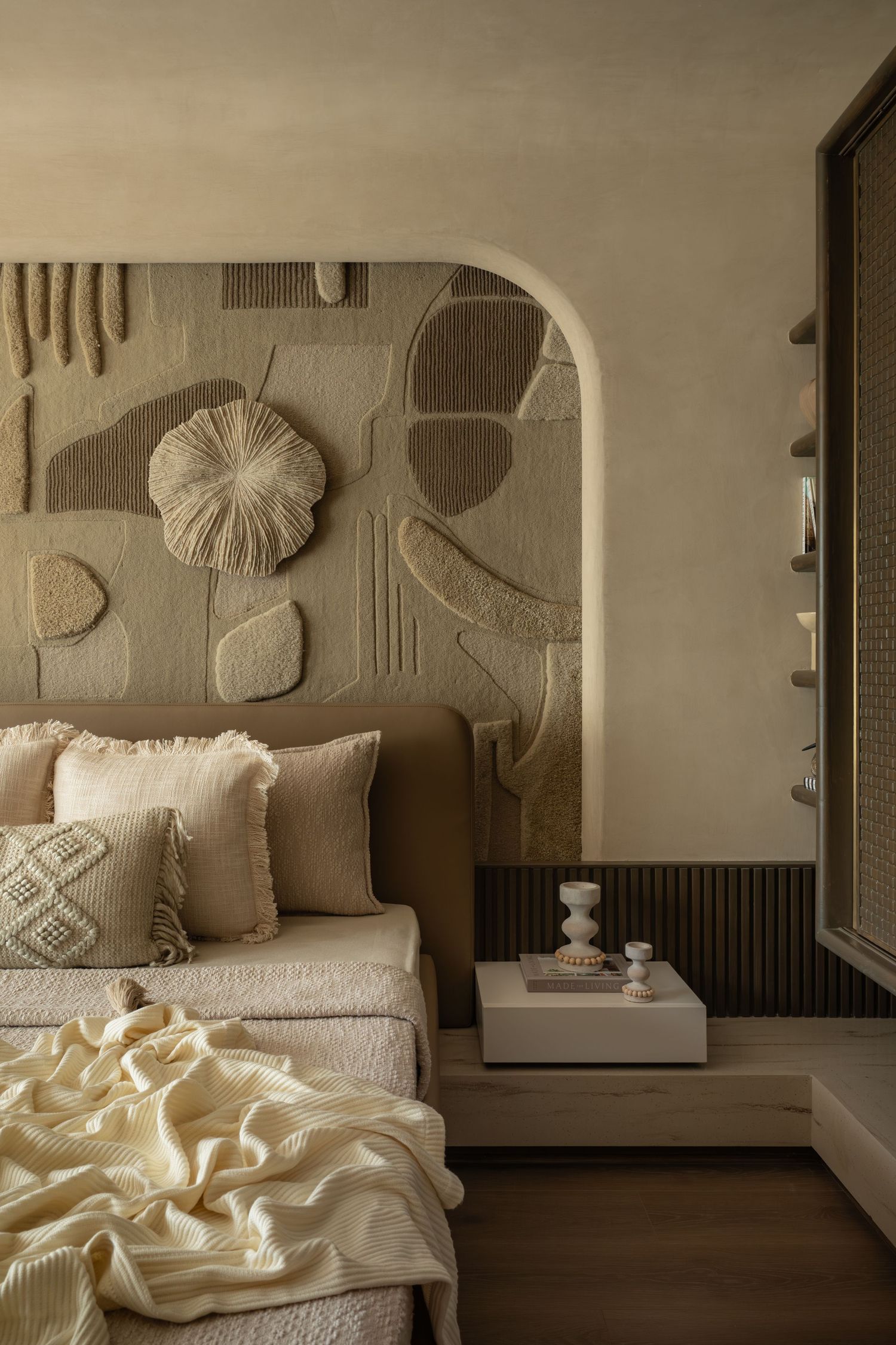 Neutral toned bedroom with textured wall art, arched headboard, layered pillows, and a cream knit throw blanket.