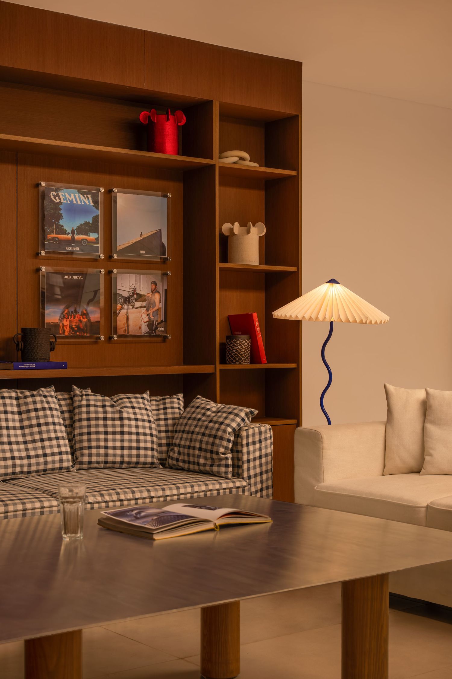 Warm living space with plaid sofa, white couch, wooden shelving, and blue wavy floor lamp.