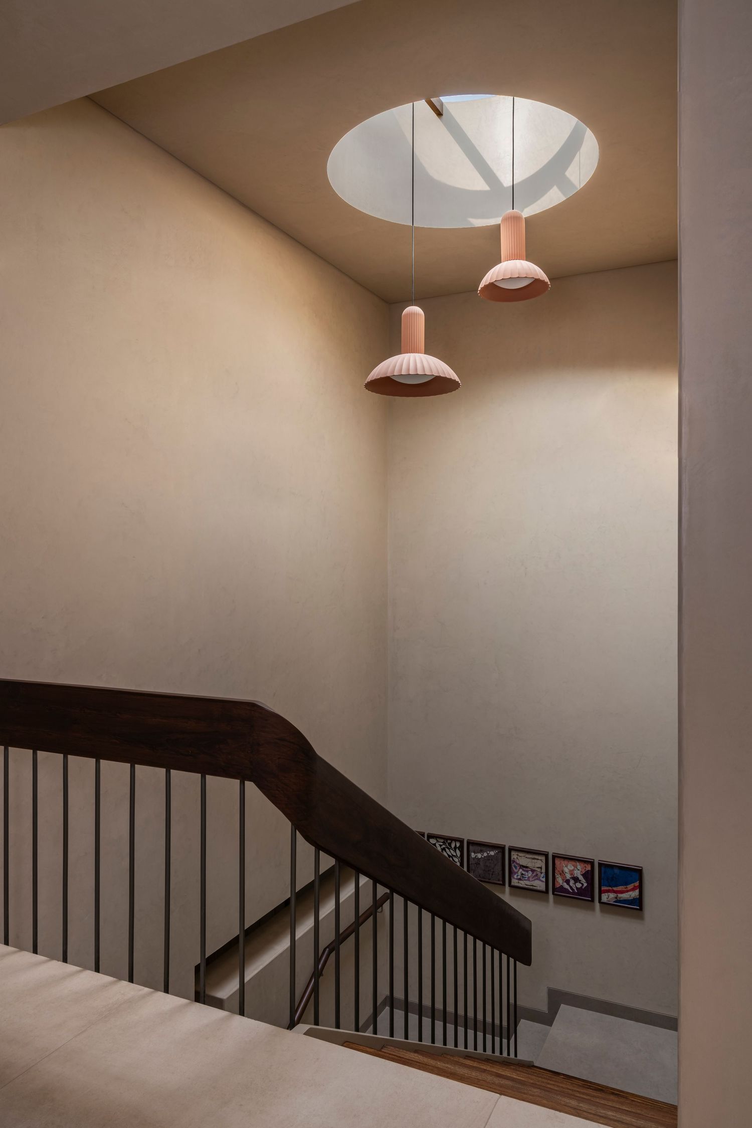 Modern staircase with dark wood handrail, black iron balusters, pink pendant lights, and a circular skylight above.