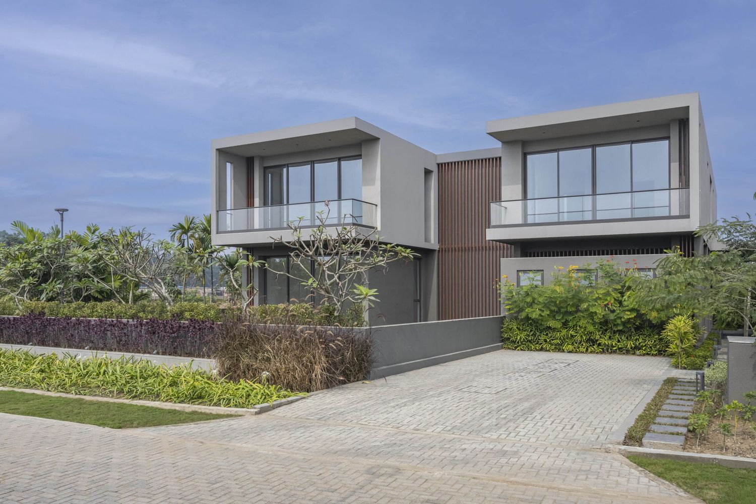 Contemporary two-story villa with glass balconies, wood cladding, and lush tropical landscaping.