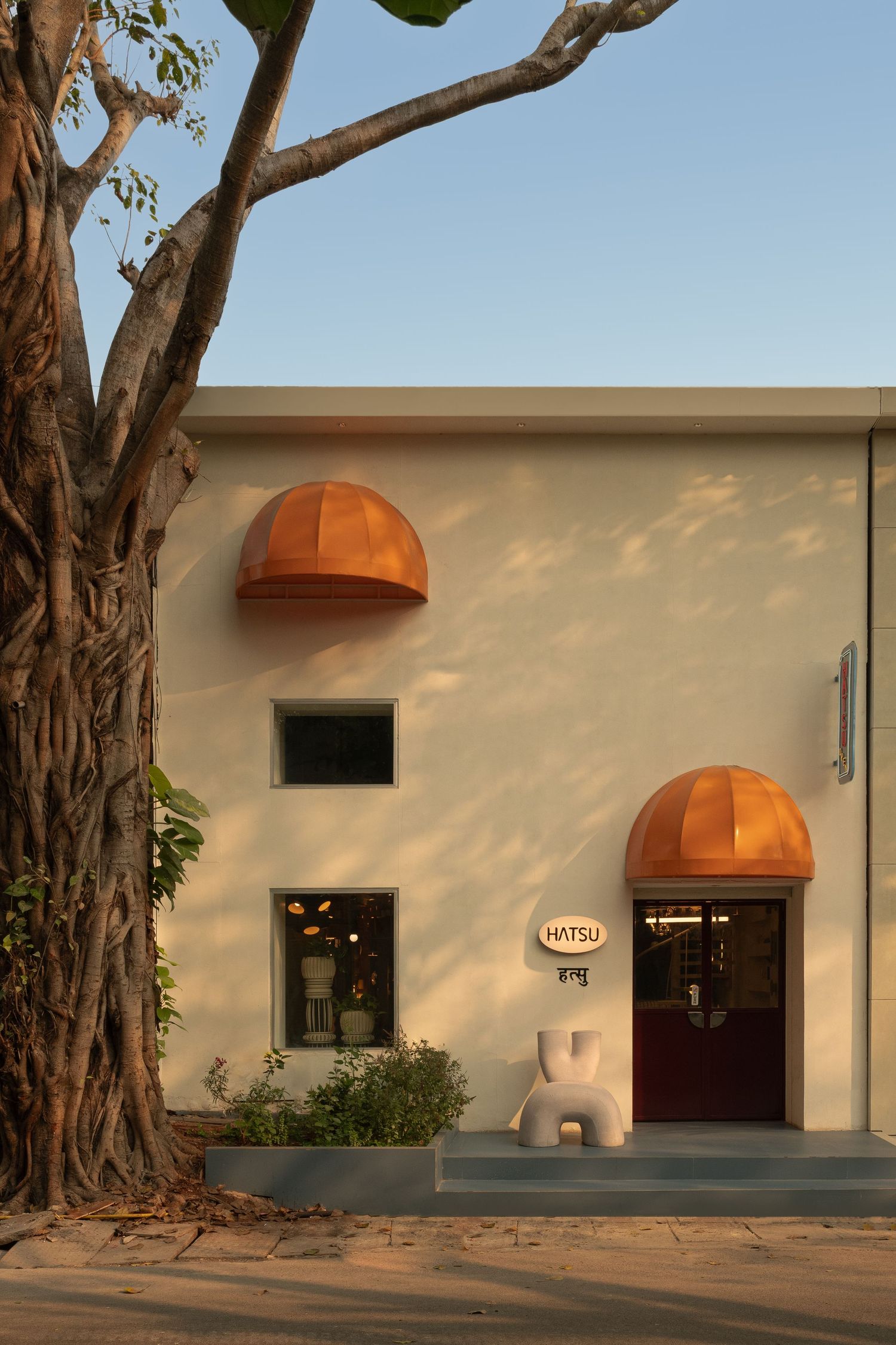 Hatsu restaurant exterior featuring distinctive copper dome awnings, white sculptural chair, and large tree.