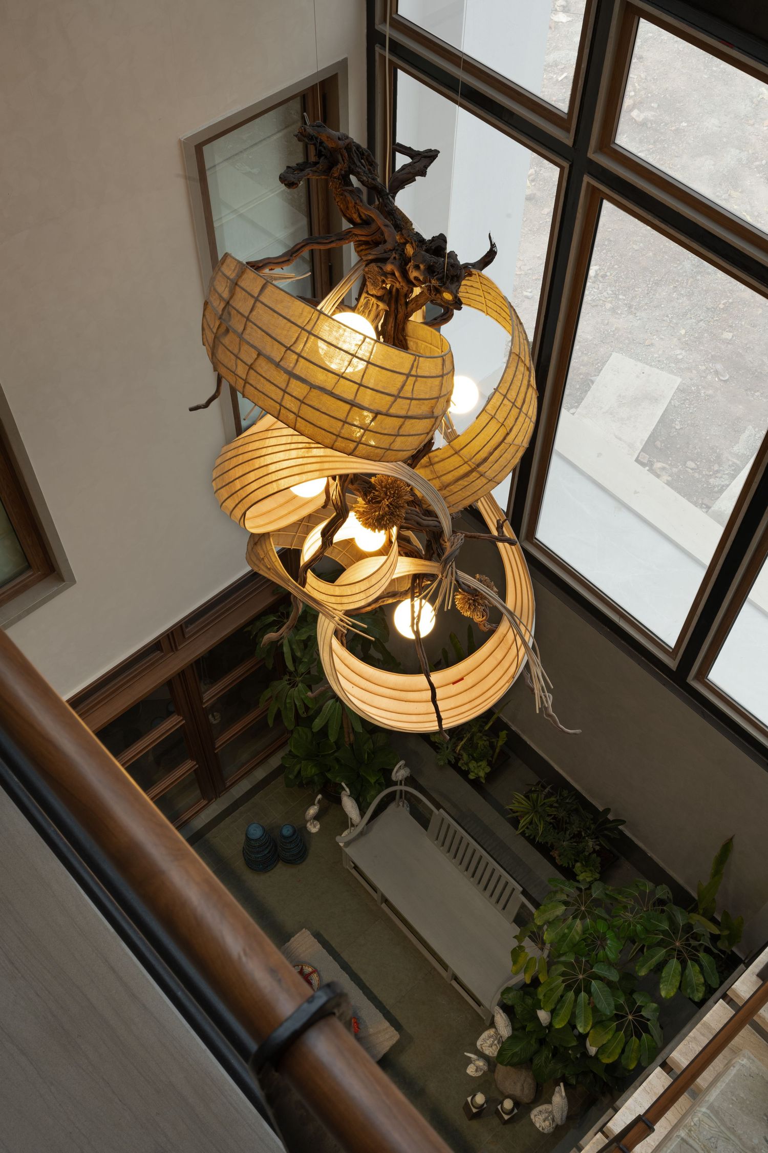 Dramatic atrium view featuring sculptural rattan pendant lights and lush indoor garden below.