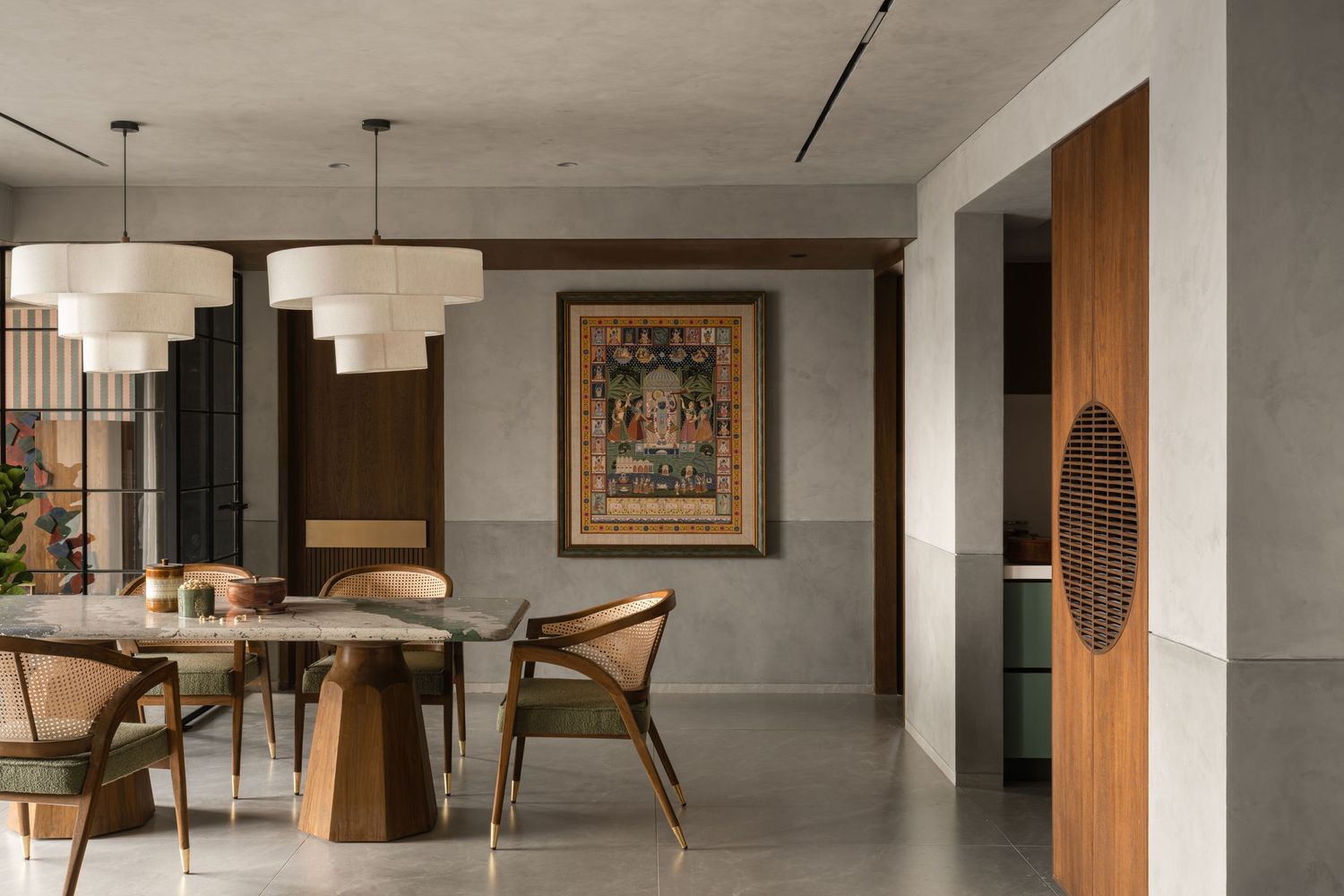 Modern dining room with glass table, wooden chairs, large framed artwork, and pendant lights in a gray interior.