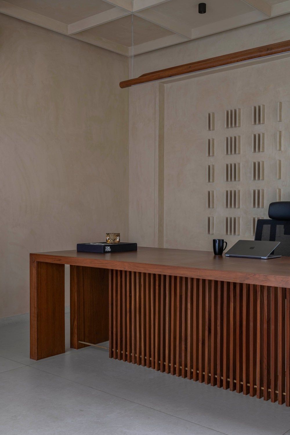 Elegant office interior featuring a walnut wood slatted executive desk with laptop and decorative wall relief panels.
