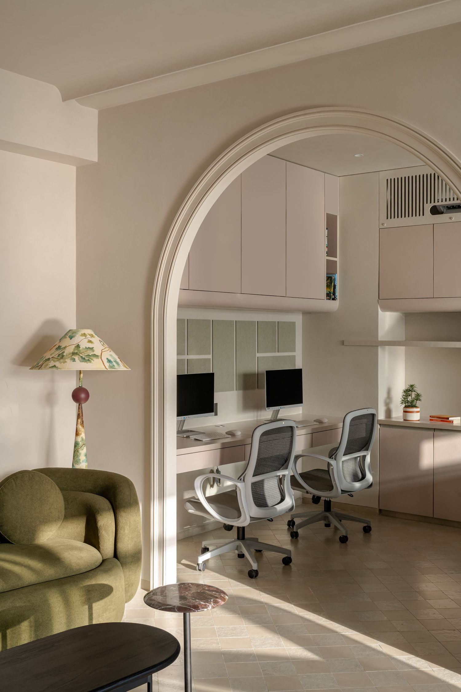 Elegant arched doorway leading to bright home office with dual monitors, white ergonomic chairs, and built-in cabinetry.