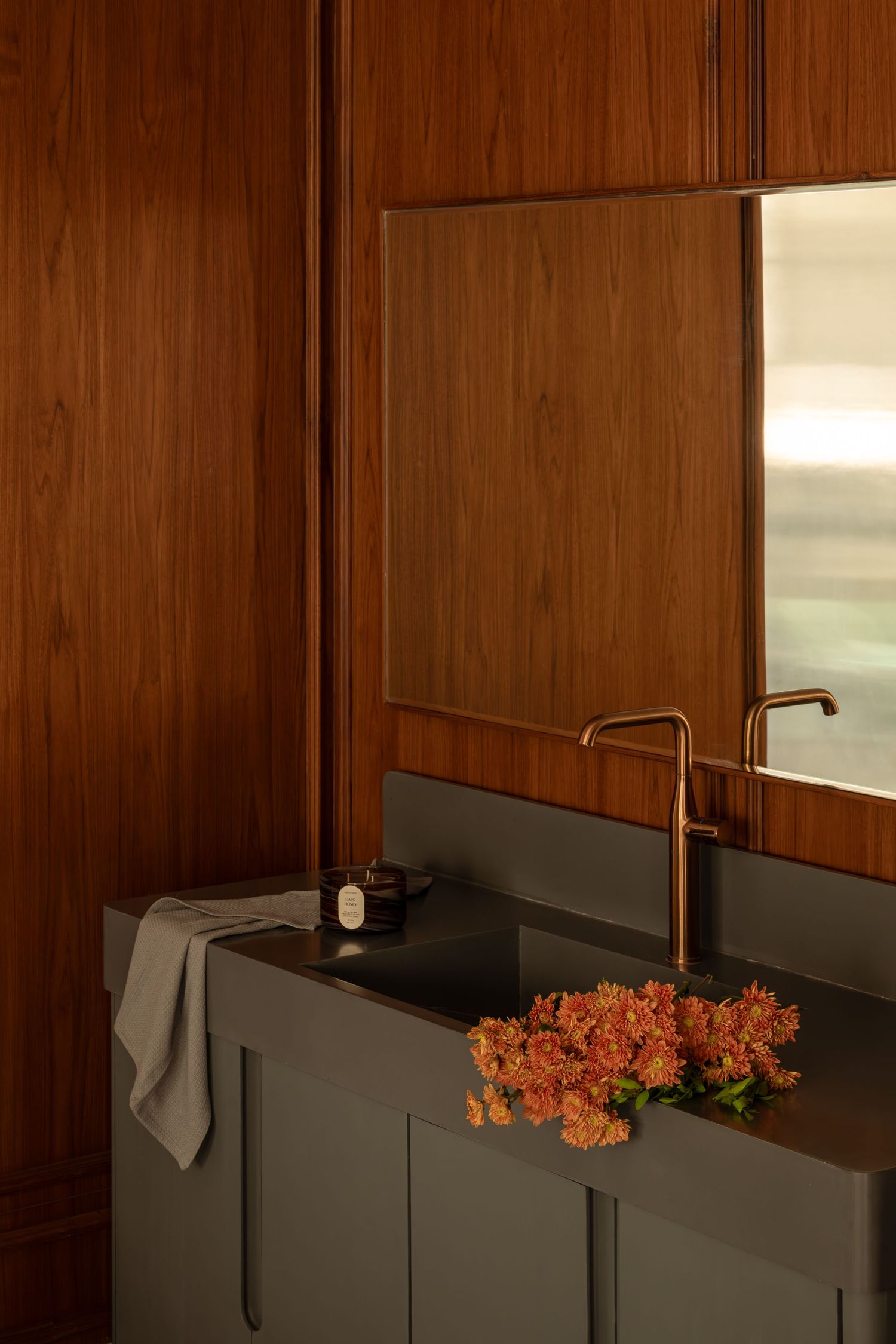 Luxury bathroom vanity with dark green cabinetry, gold faucet, and rich walnut wood wall paneling.