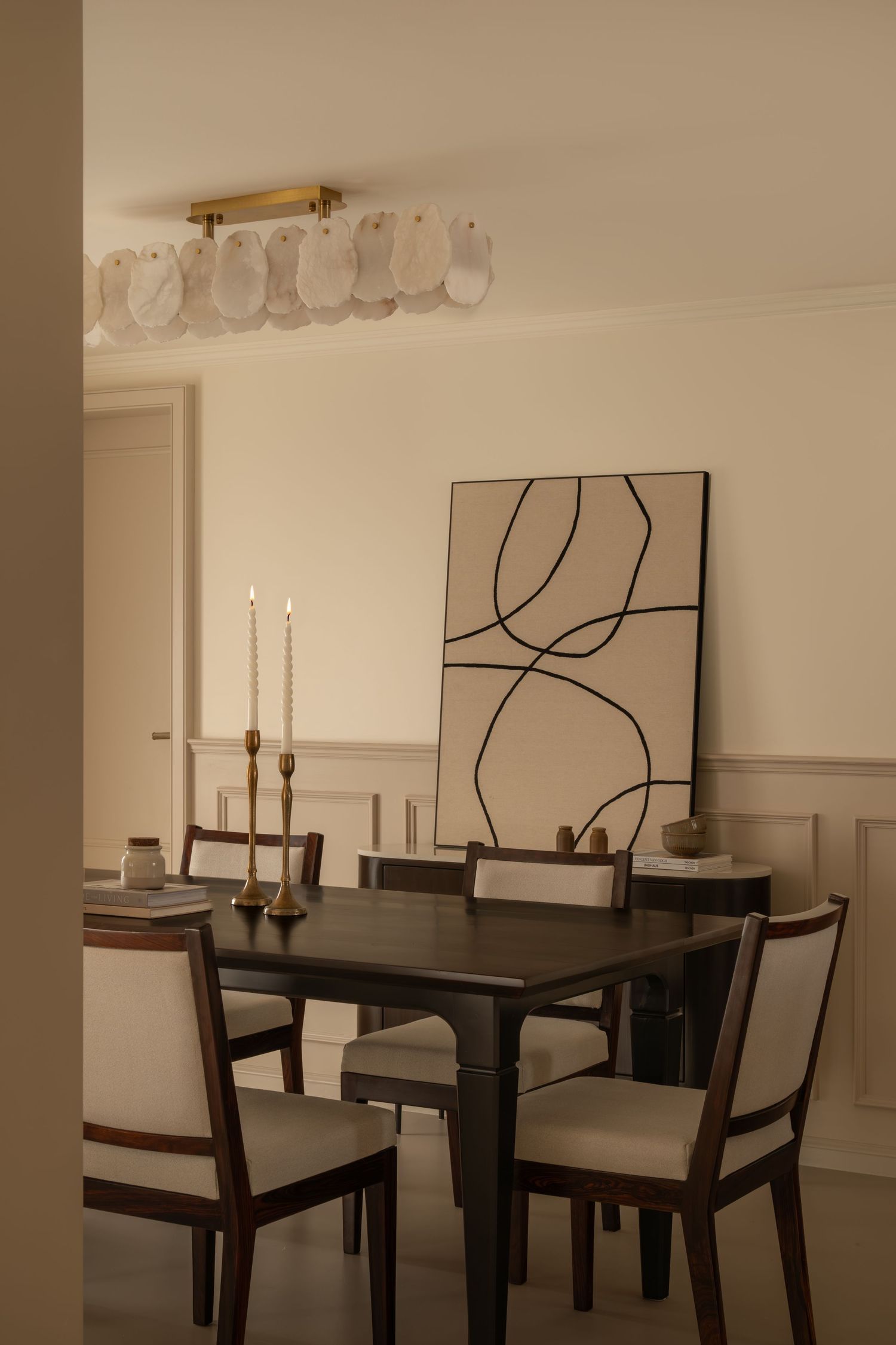 Intimate dining room with dark wood table, upholstered chairs, tapered candles, and abstract wall art.