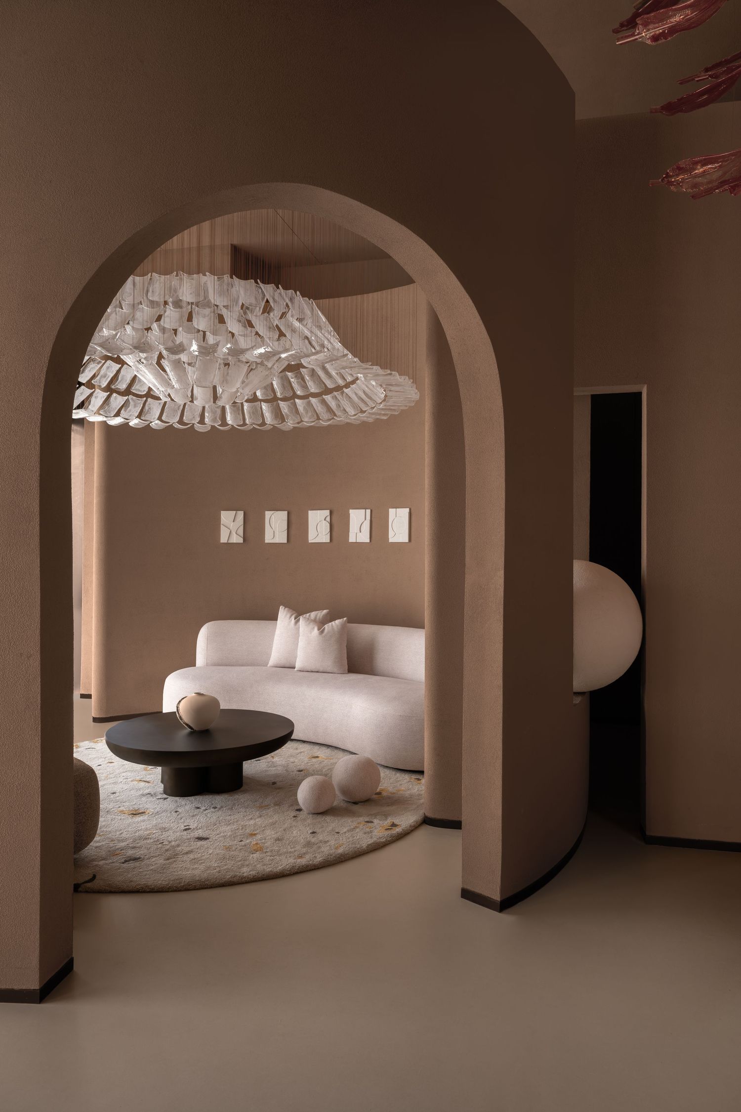 Elegant neutral-toned living room with arched doorway, white curved sofa, dark coffee table, and sculptural pendant light.