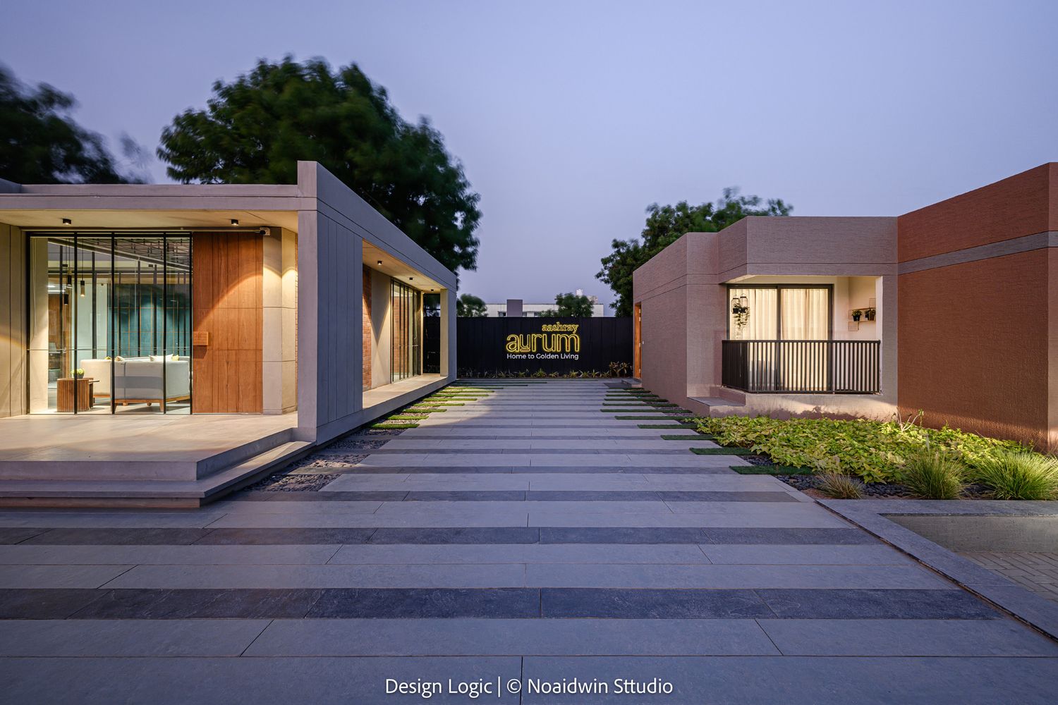 Two modern pavilion structures flanking a wide stone pathway with landscaped borders illuminated at dusk.