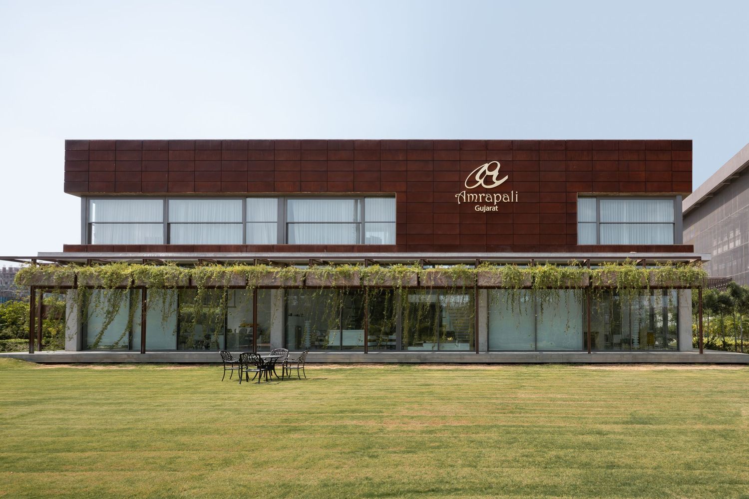 Modern two-story building with wood facade, green rooftop plants, glass windows, and manicured lawn seating area.