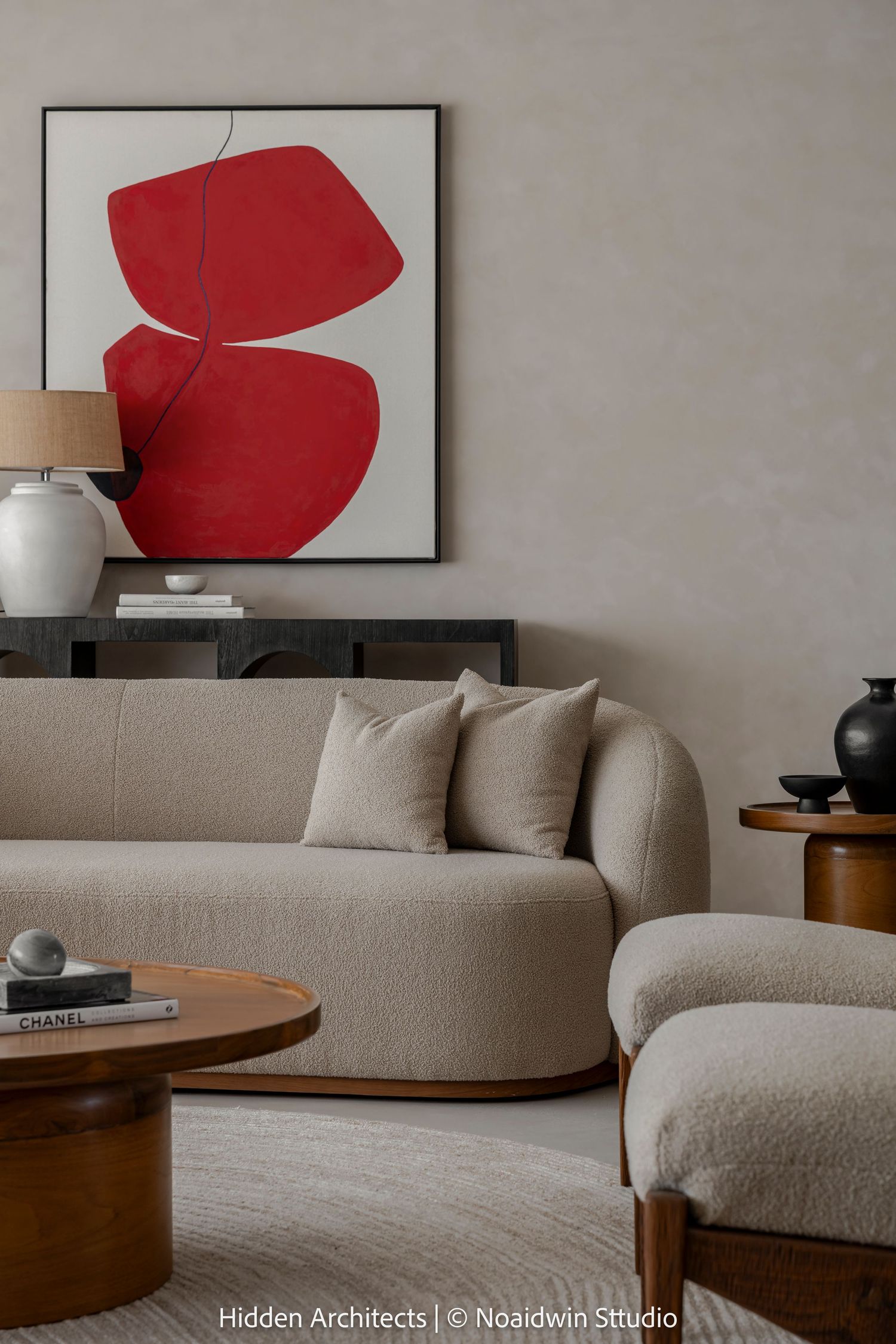 Stylish living room with curved beige bouclé sofa, red abstract wall art, ceramic lamp, and round walnut coffee table.