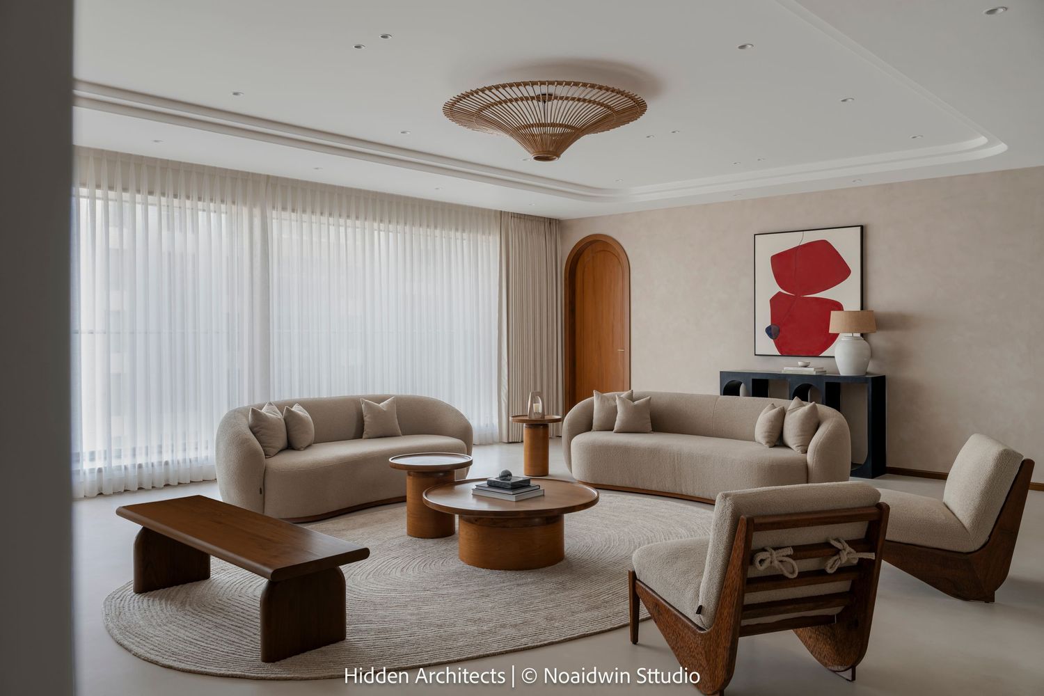 Spacious modern living room featuring curved beige sofas, round coffee tables, red abstract art, and floor-to-ceiling sheer curtains.