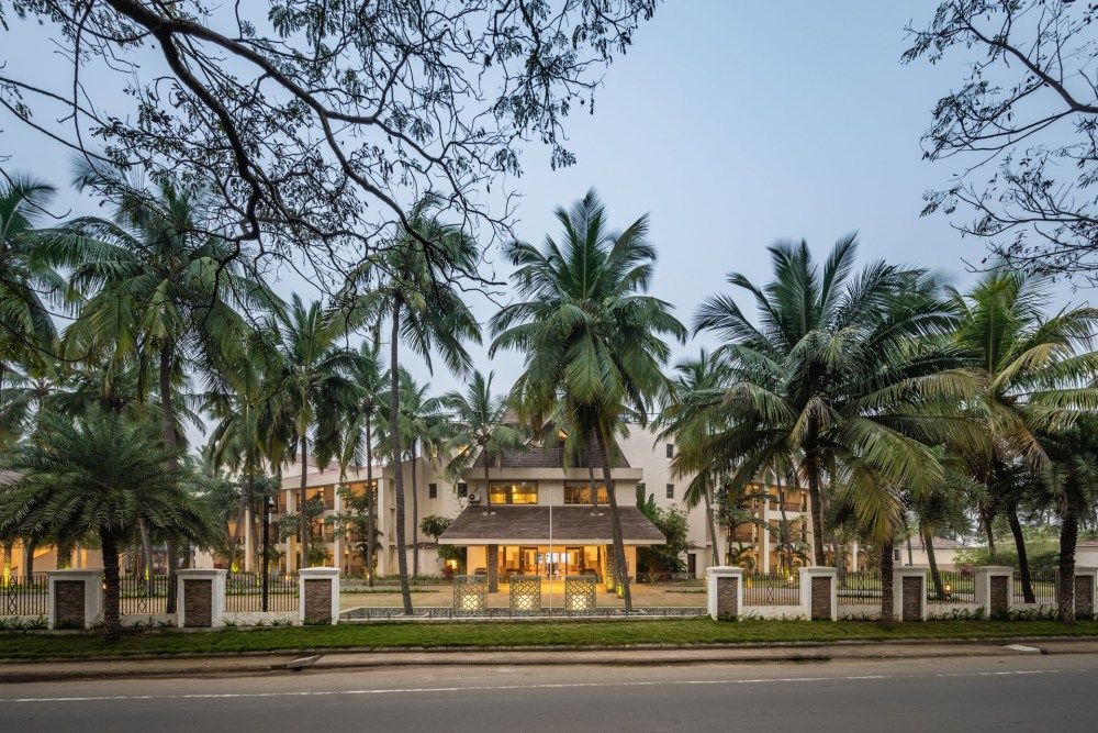 Hotel entrance surrounded by tall palm trees and a white fence along a quiet road.