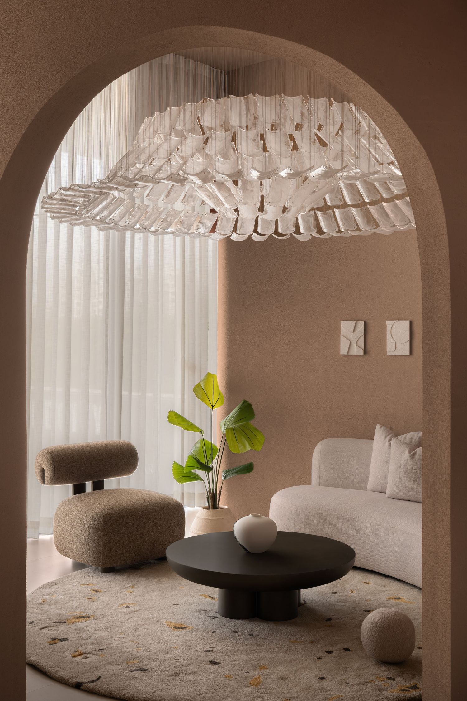 Elegant living room with arched doorway, sculptural chandelier, bouclé sofa, dark coffee table, and neutral tones.